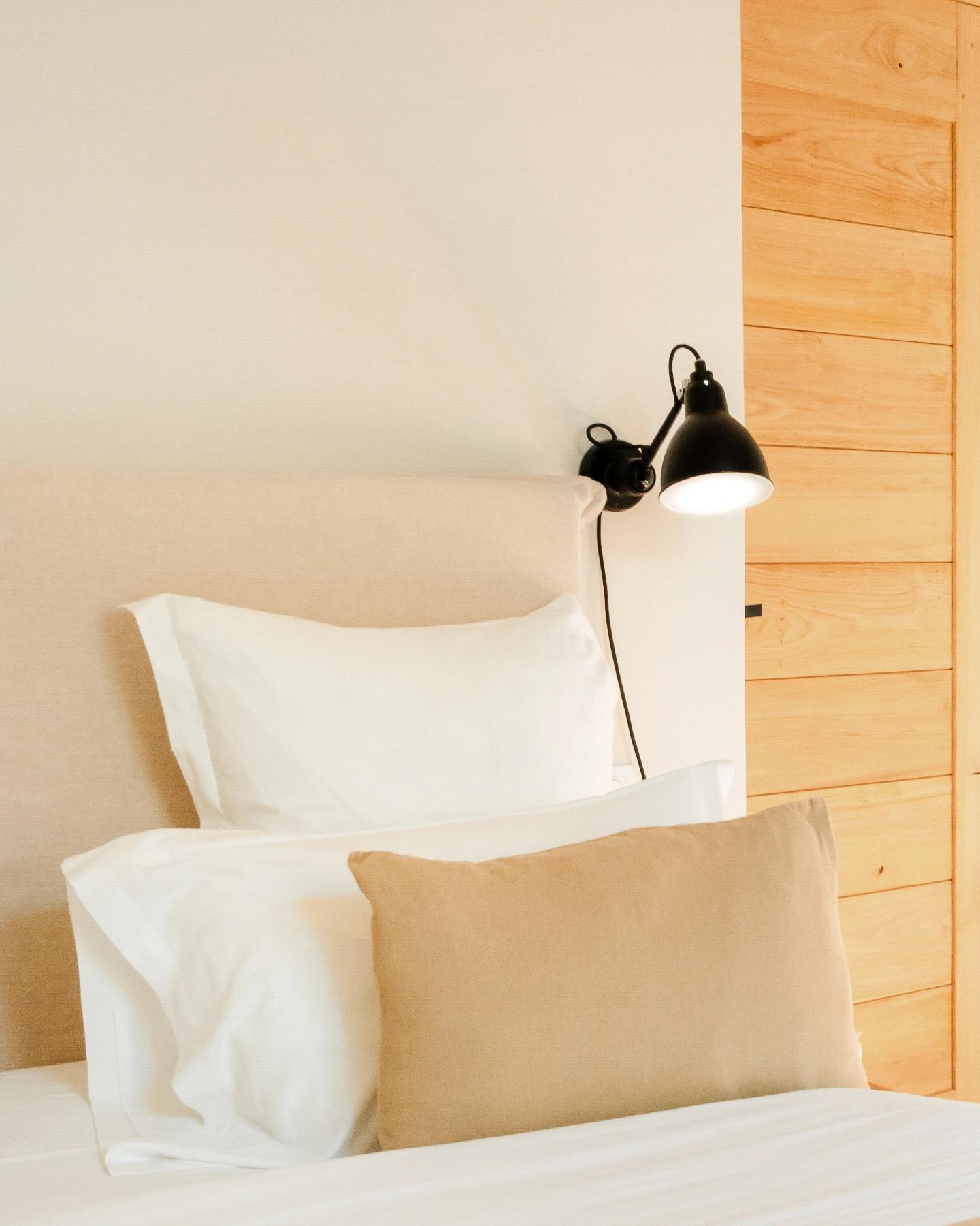 Lit aux coussins clairs sous une applique murale